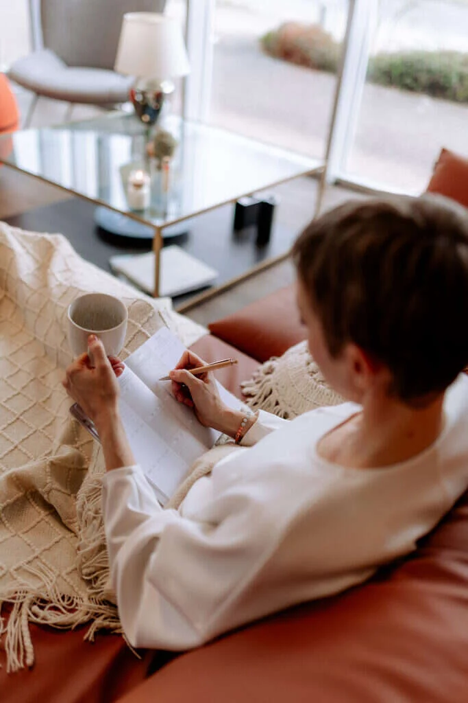Frau notiert mit einer Tasse in der Hand Termine in ihren Kalender.