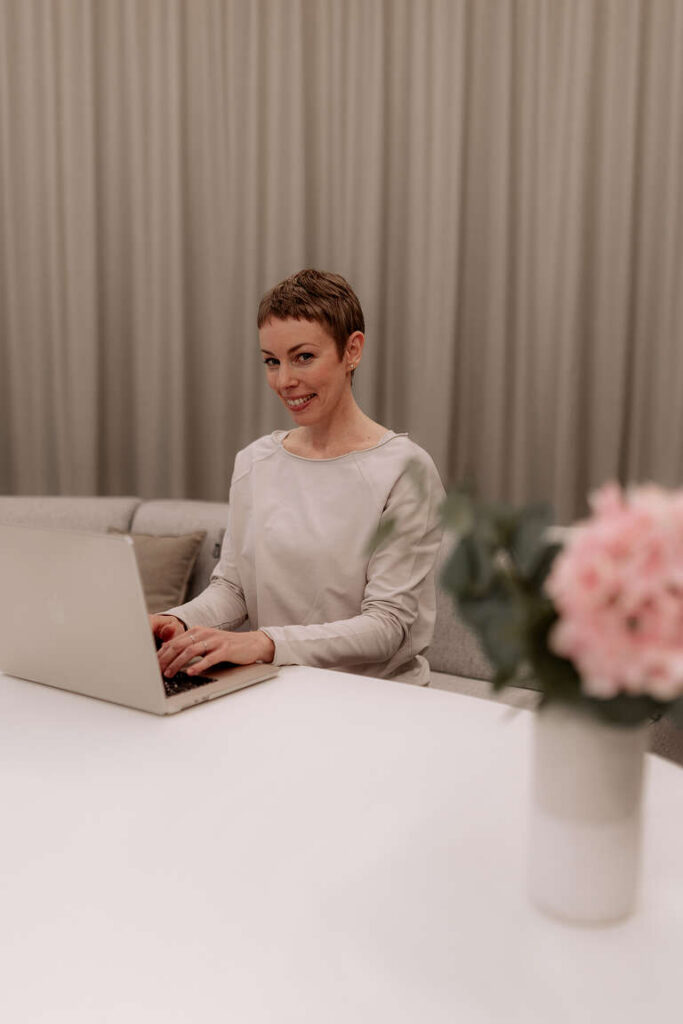 Stephanie Hartdegen sitzt lächelnd am Schreibtisch und arbeitet am Laptop.